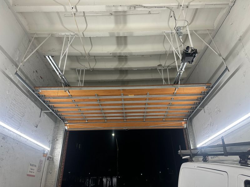 Commercial wood overhead door open at night showing interior with work van and track system